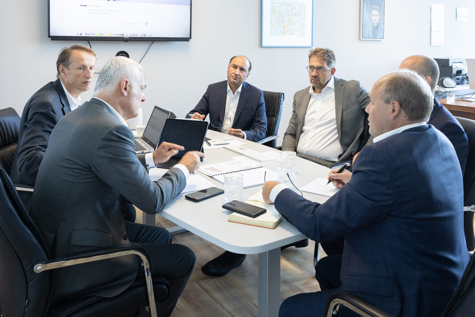 Geschäftsleute besprechen sich an einem runden Tisch mit Laptops und Notizbüchern in einem modernen Büro.